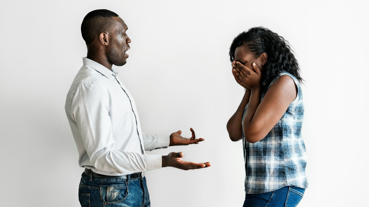 A man gestures with open hands while a woman stands across from him covering her face.
