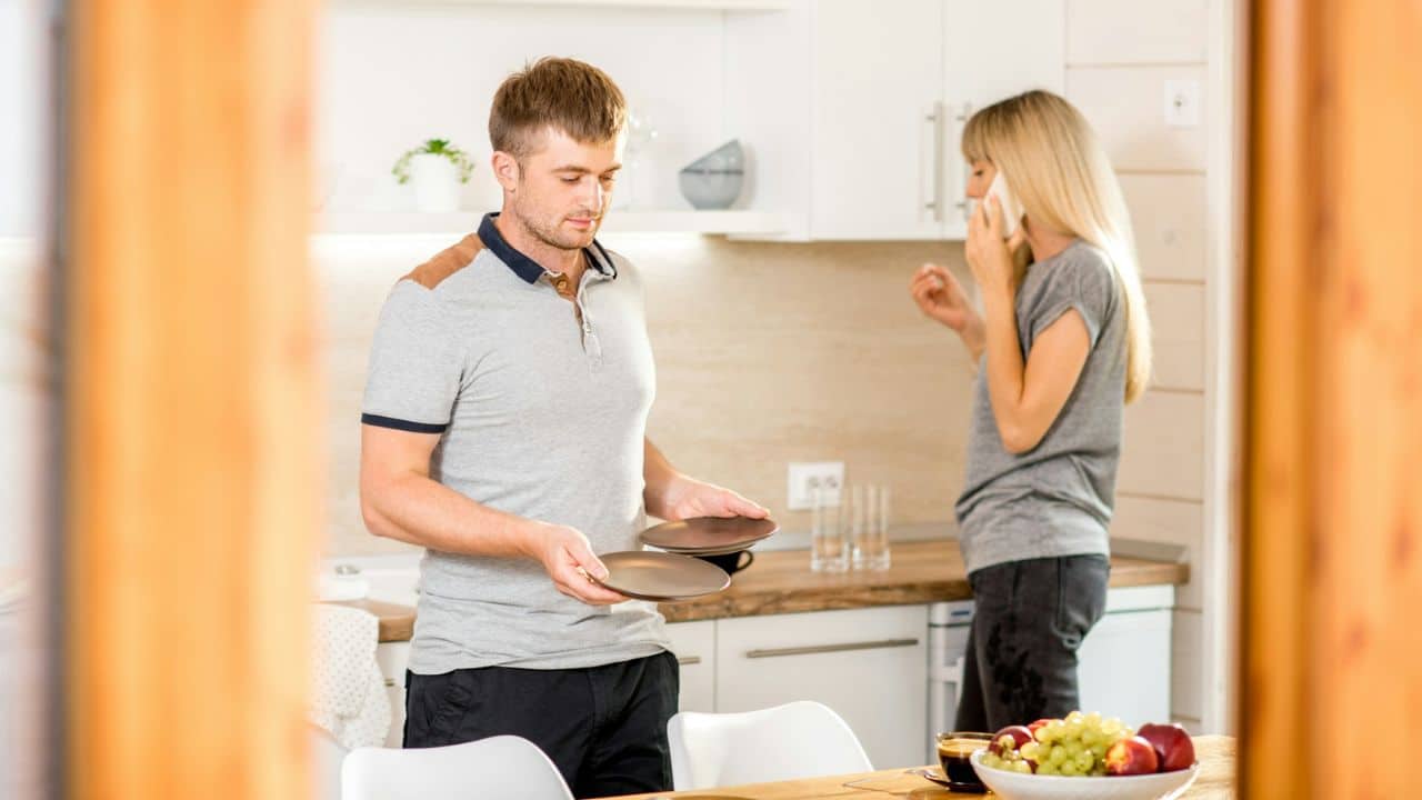 A man holds two plates while a woman in the background talks on a cell phone.