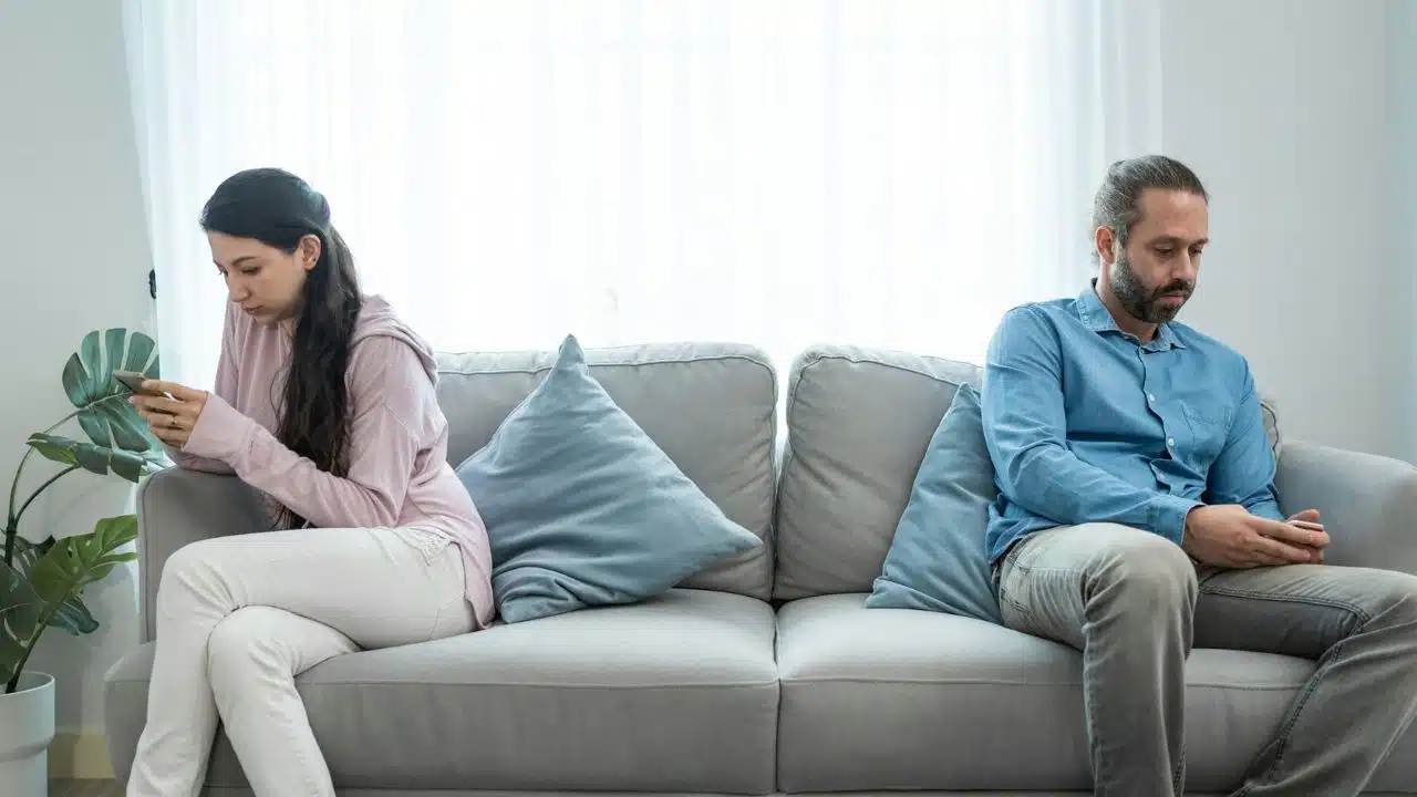 A man and woman sit at opposite ends of a couch using their phones.
