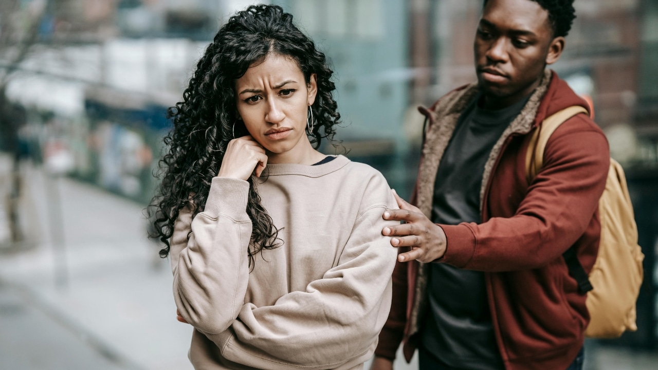A woman with a concerned expression looks away while a man places a hand on her.