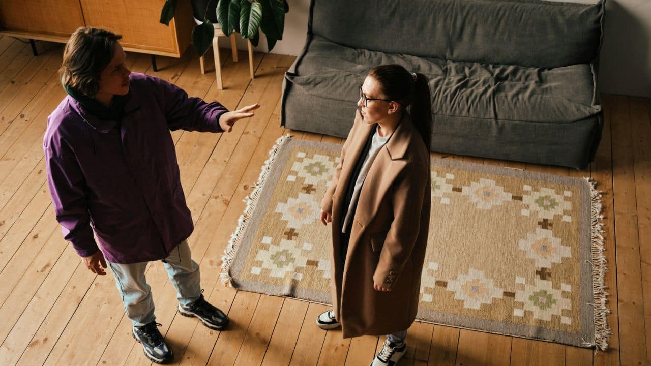 A man in a purple jacket gestures with one hand toward a woman in a coat.