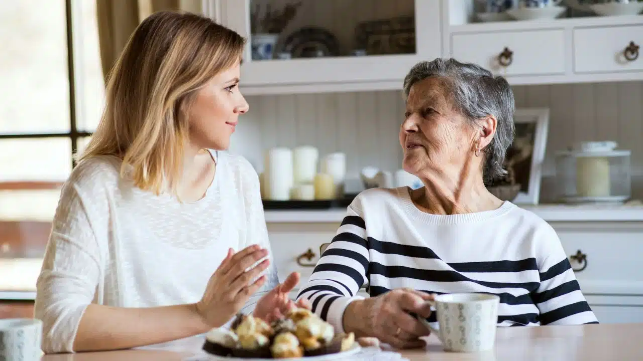 A younger woman and an older woman sit at a table talking over tea.