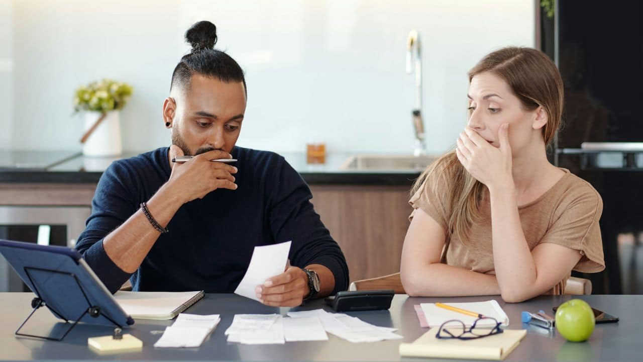 A man and woman sit at a table looking at several papers and a digital tablet.