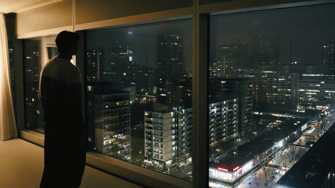 A person's silhouette stands in front of a large window overlooking a glowing city at night.