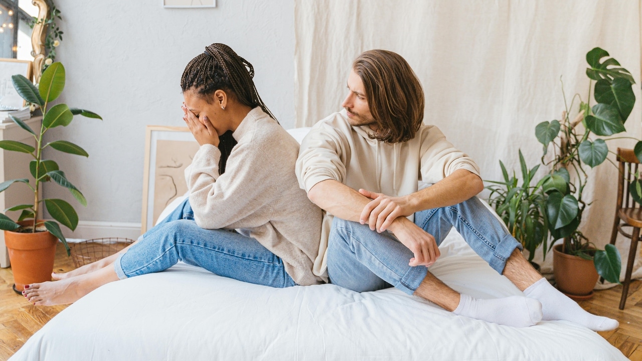 A woman sits with her face in her hands while a man looks back at her.