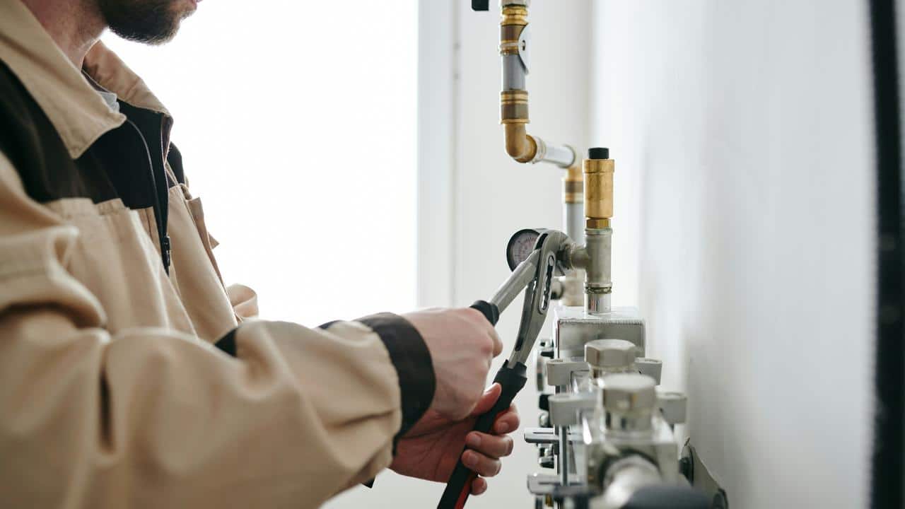 A person using a wrench to adjust pipes and a pressure gauge on a wall.