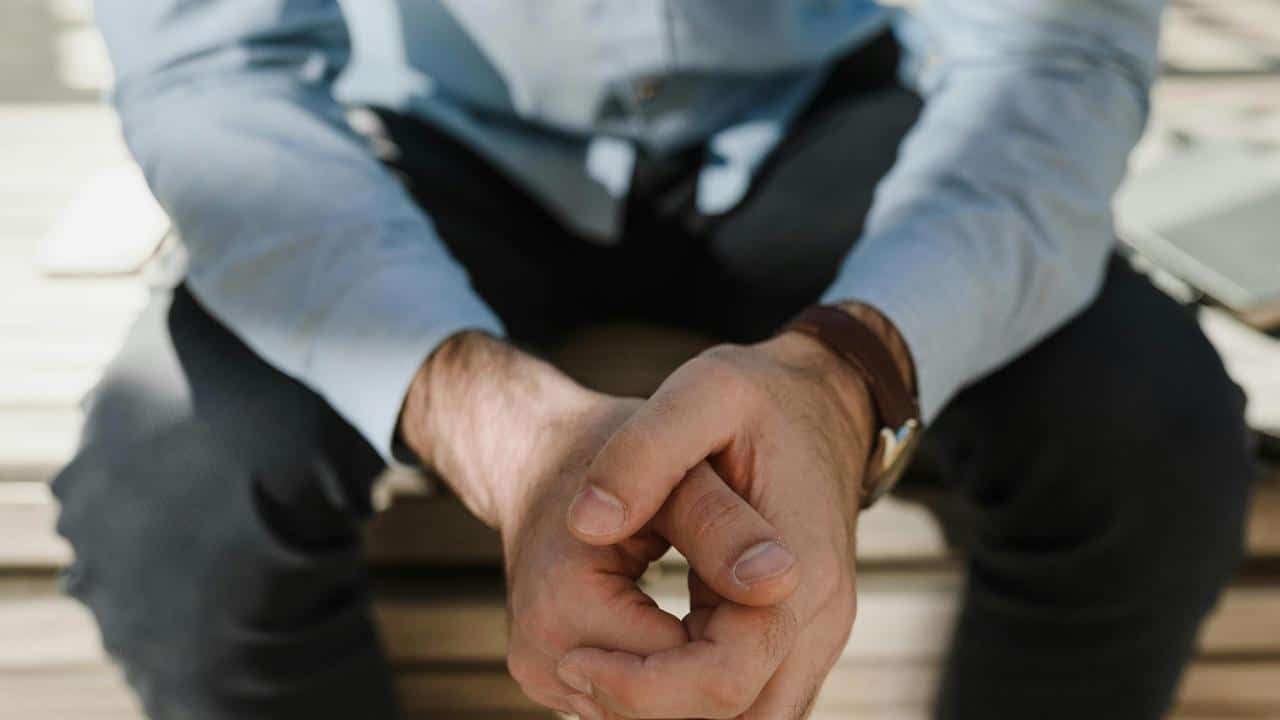 A close-up of a man sitting with his hands clasped together.