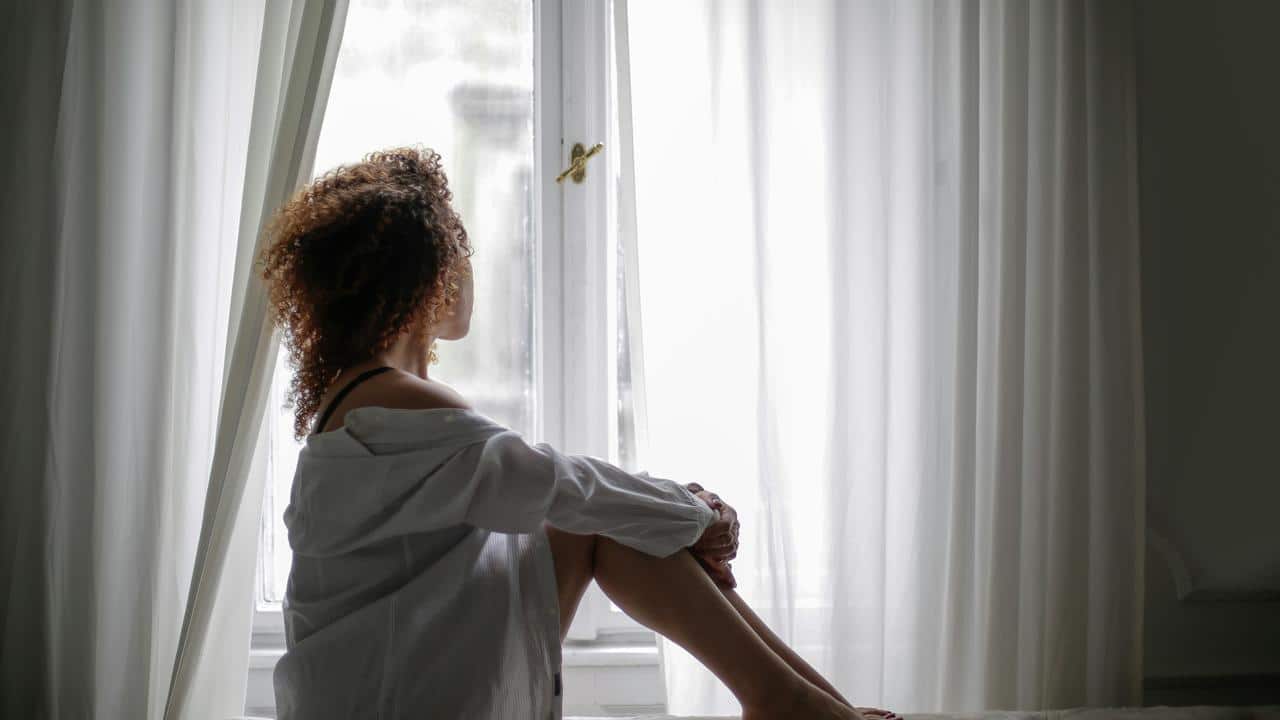 A woman sitting by a window, looking outside.