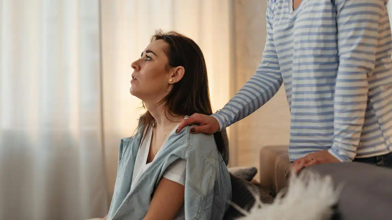 A woman sitting while another person rests a hand on her shoulder.