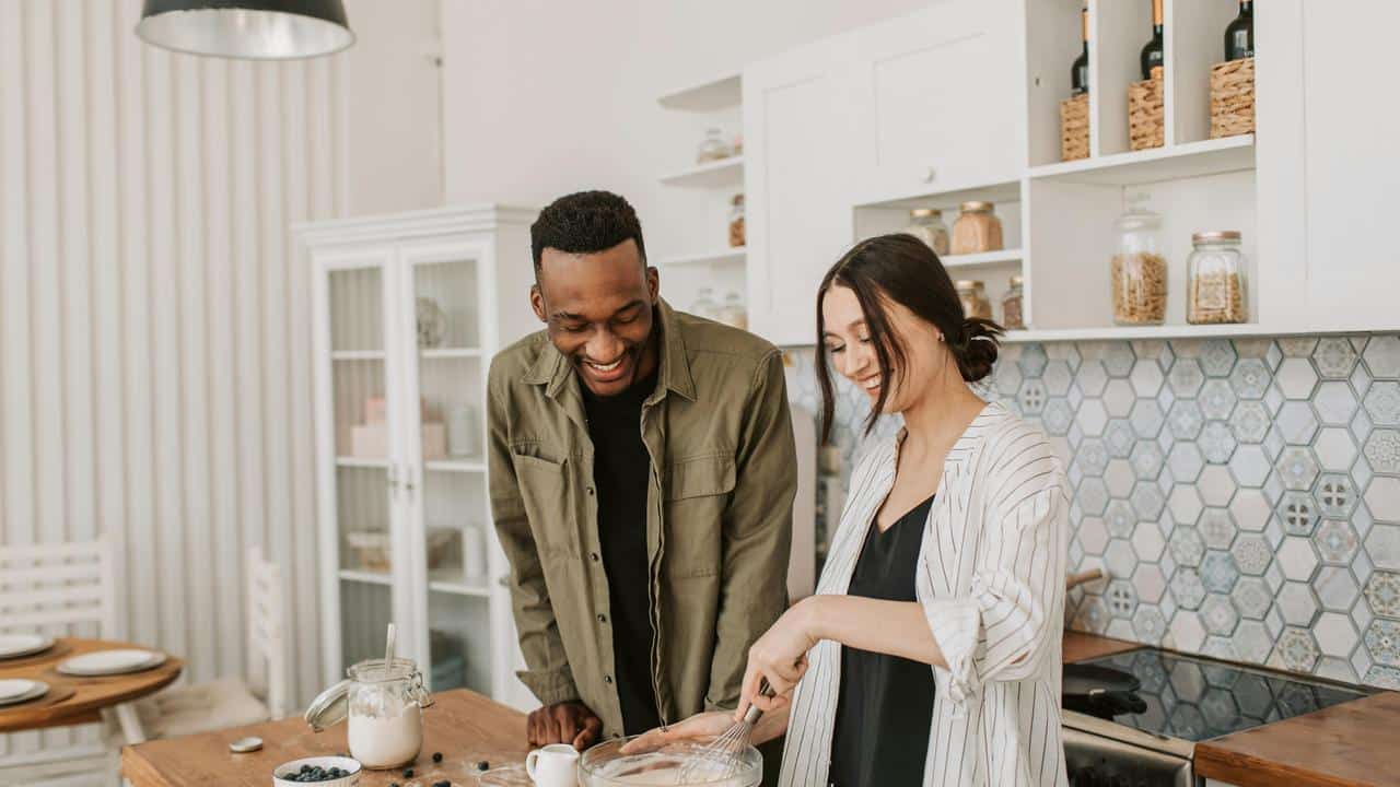 A couple smiling and cooking together in a cozy kitchen.