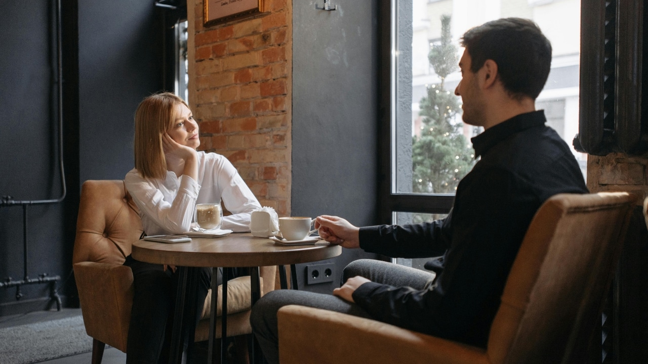 Woman in a white shirt sitting at a café table opposite a man in black.