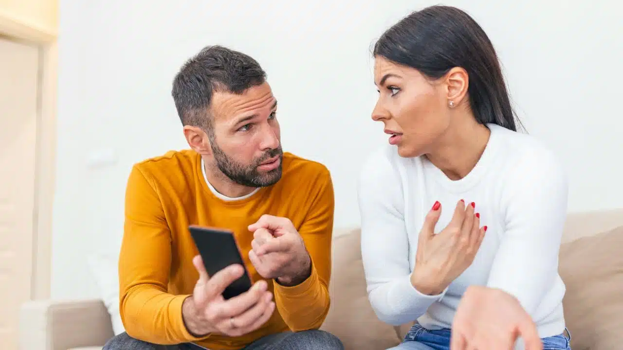 A man points at a smartphone screen while talking to a woman with a concerned expression.