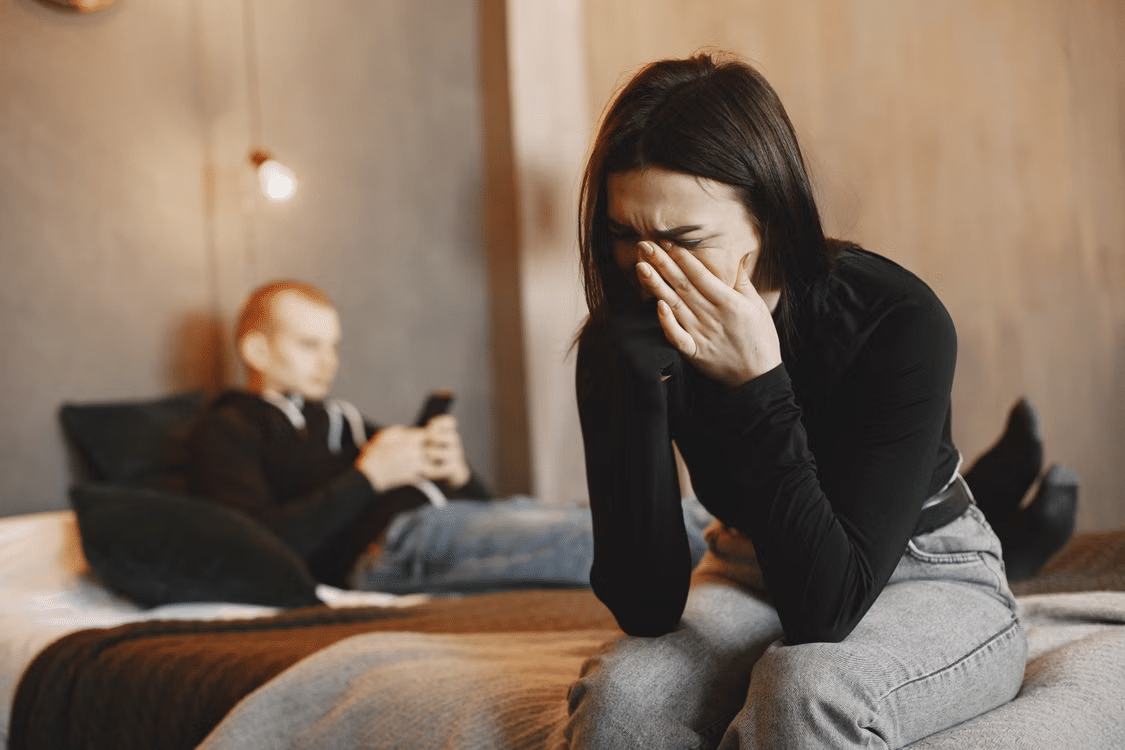 A woman crying while a man sits unbothered in the background.