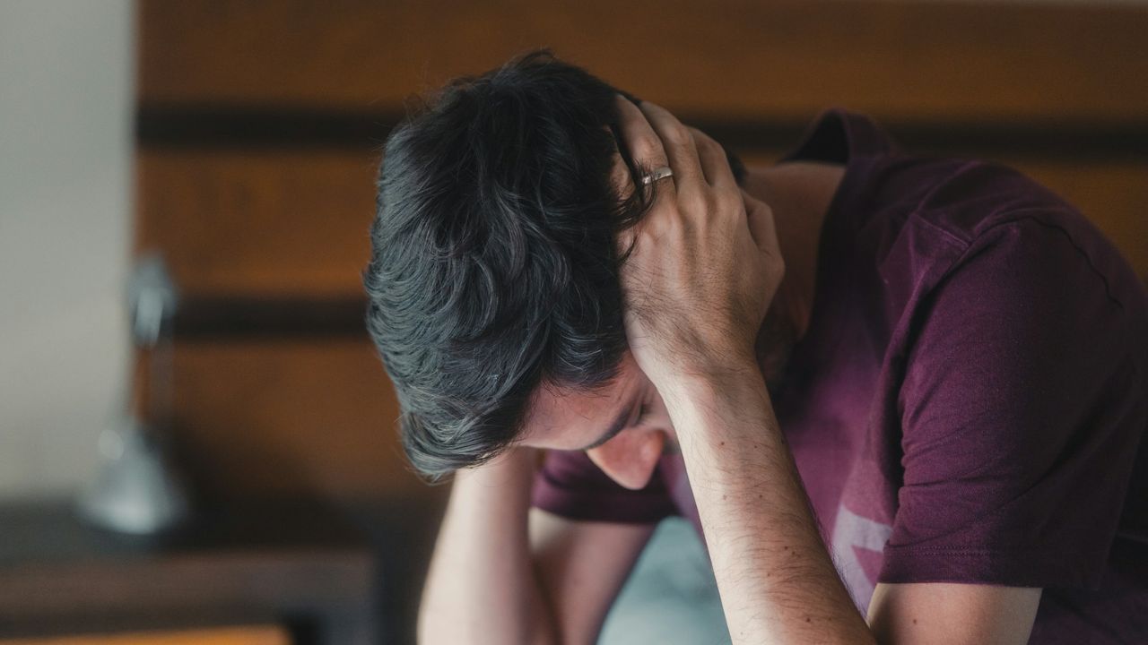 A distraught man holding his head with both hands, looking upset or in pain.