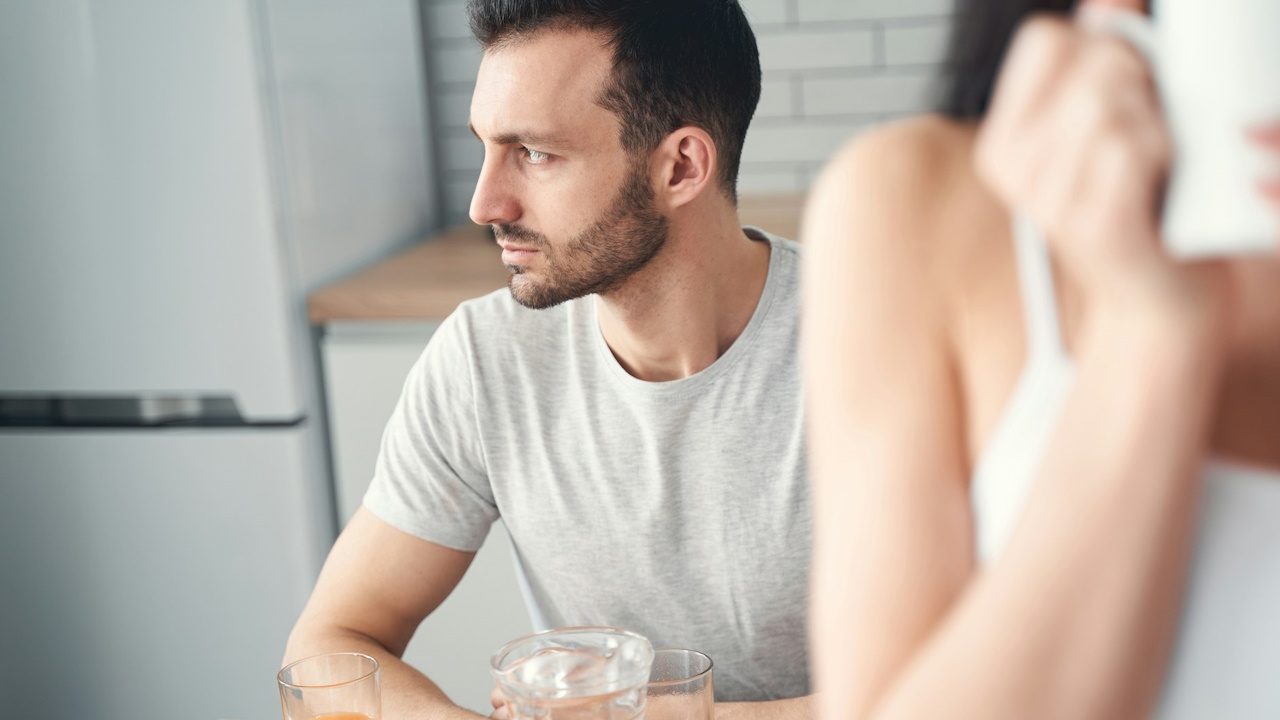 A thoughtful man looking away while his wife is talking on the phone.