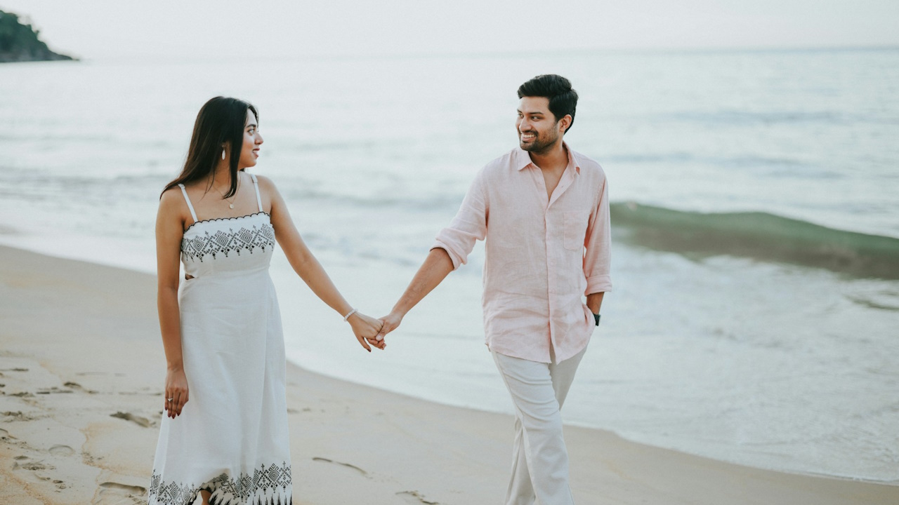 A couple holding hands walking on a beach.