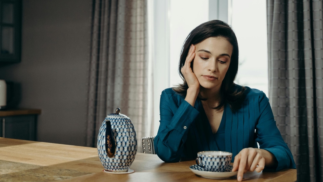 A woman in a blue blouse sits at a table near a patterned tea set.