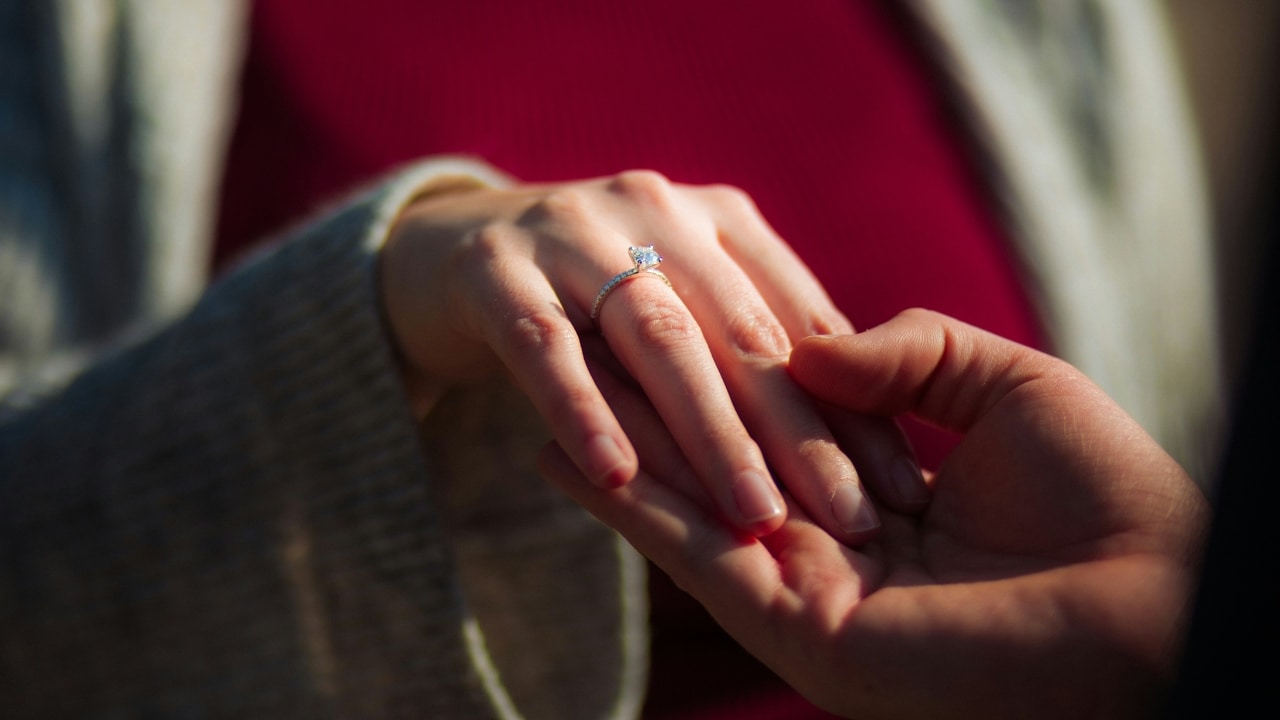 Close up of a person's hand wearing a diamond ring resting on another person's open palm.