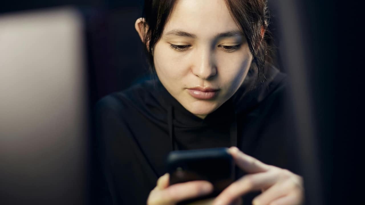 A close-up shot of a woman looking down at the screen of a handheld mobile phone.