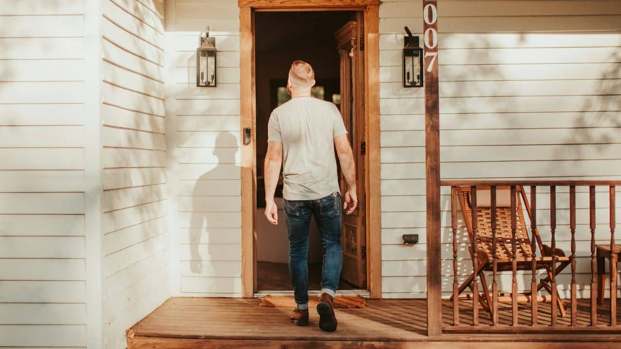 A man in a t-shirt and jeans walks through an open doorway into a house.