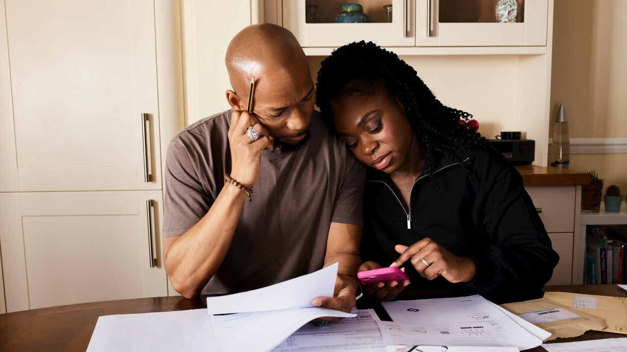 A man and woman sitting at a table together, looking closely at several paper documents.