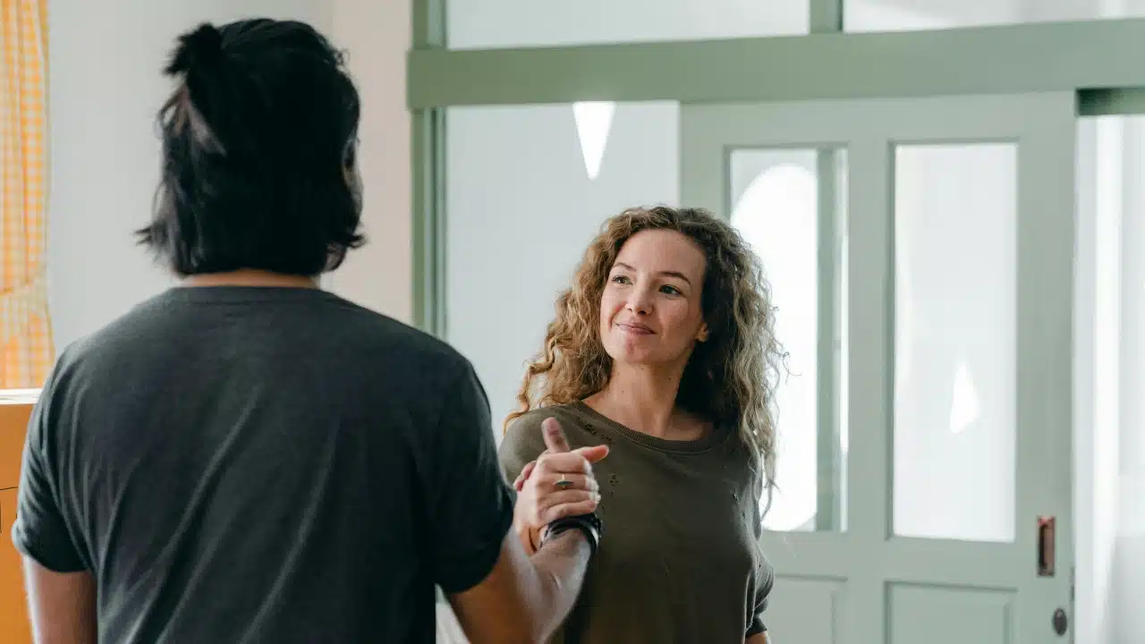 A woman with curly hair smiles while holding hands with a man seen from behind.
