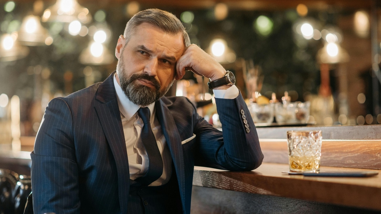 A man in a suit leans his head on his hand at a bar counter.