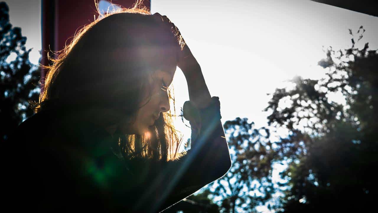 A woman silhouetted against bright light, holding her head in thought.
