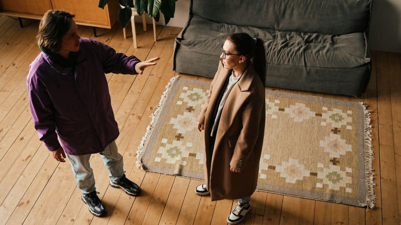 An overhead view of two women arguing in a living room with wooden floors.