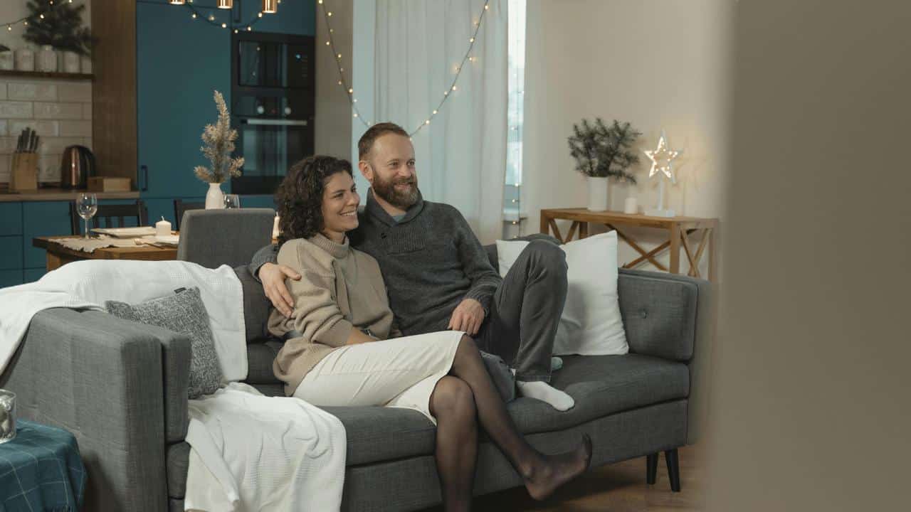 A couple sitting close together on a couch, smiling in a cozy living room.