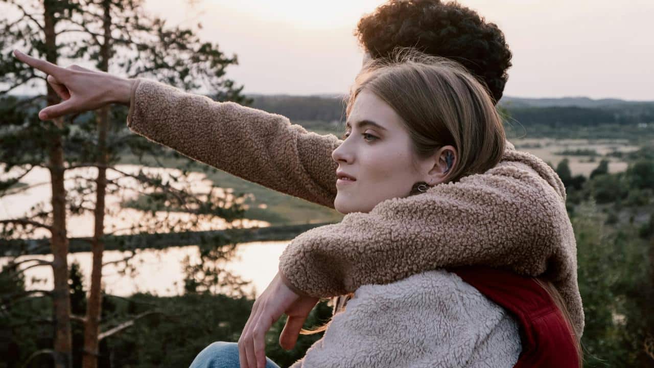 A couple sitting outdoors at sunset, with one person pointing into the distance.