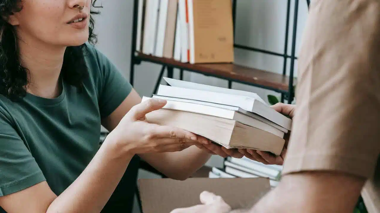 A person handing a stack of books to another person.