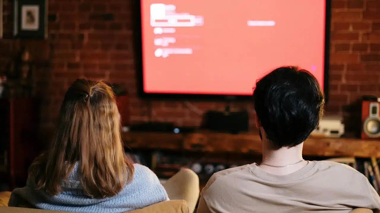 A couple sitting on a couch watching a TV screen.