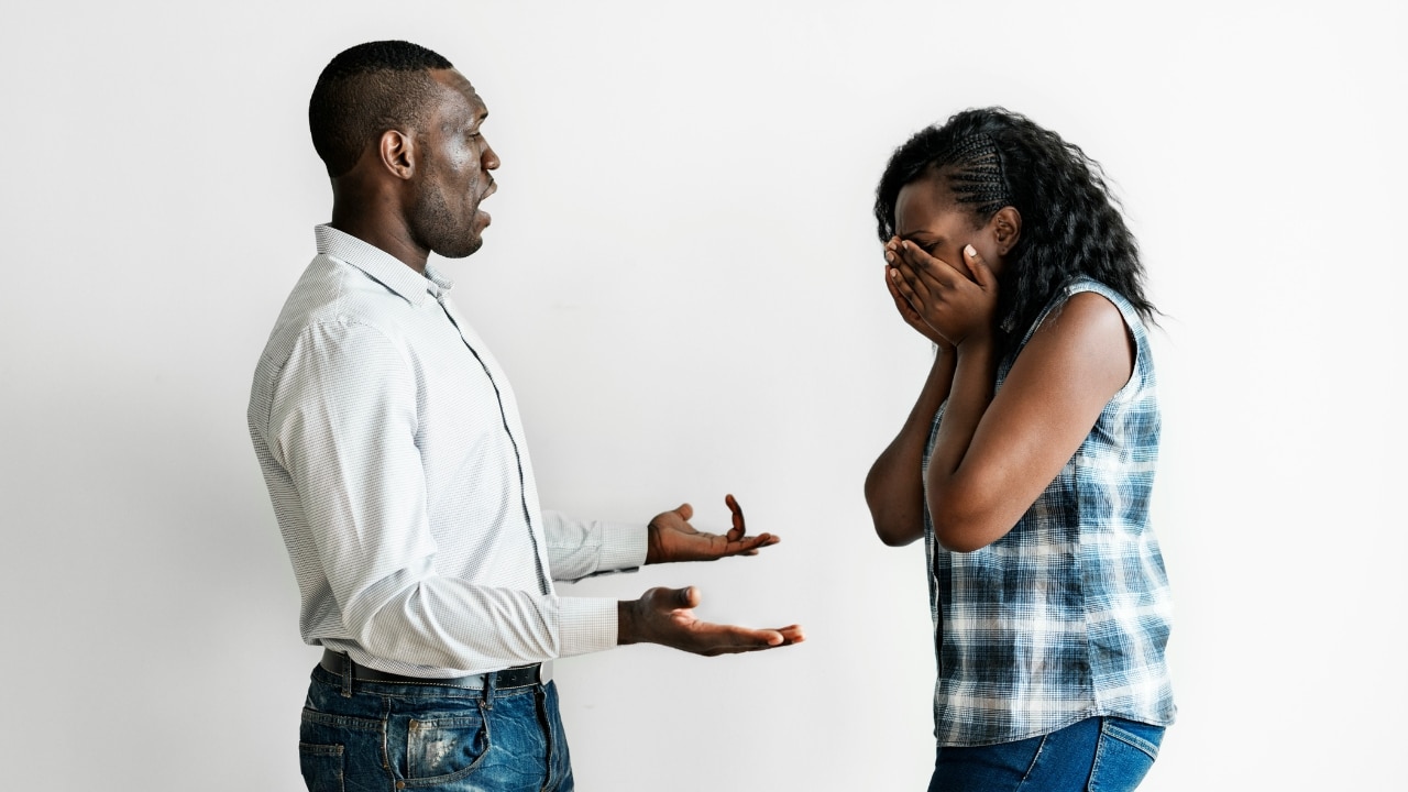 A man stands and speaks to a woman who is covering her face with hands.
