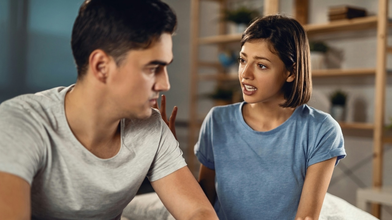 A woman in a blue shirt speaks animatedly to a man who is looking away from her.