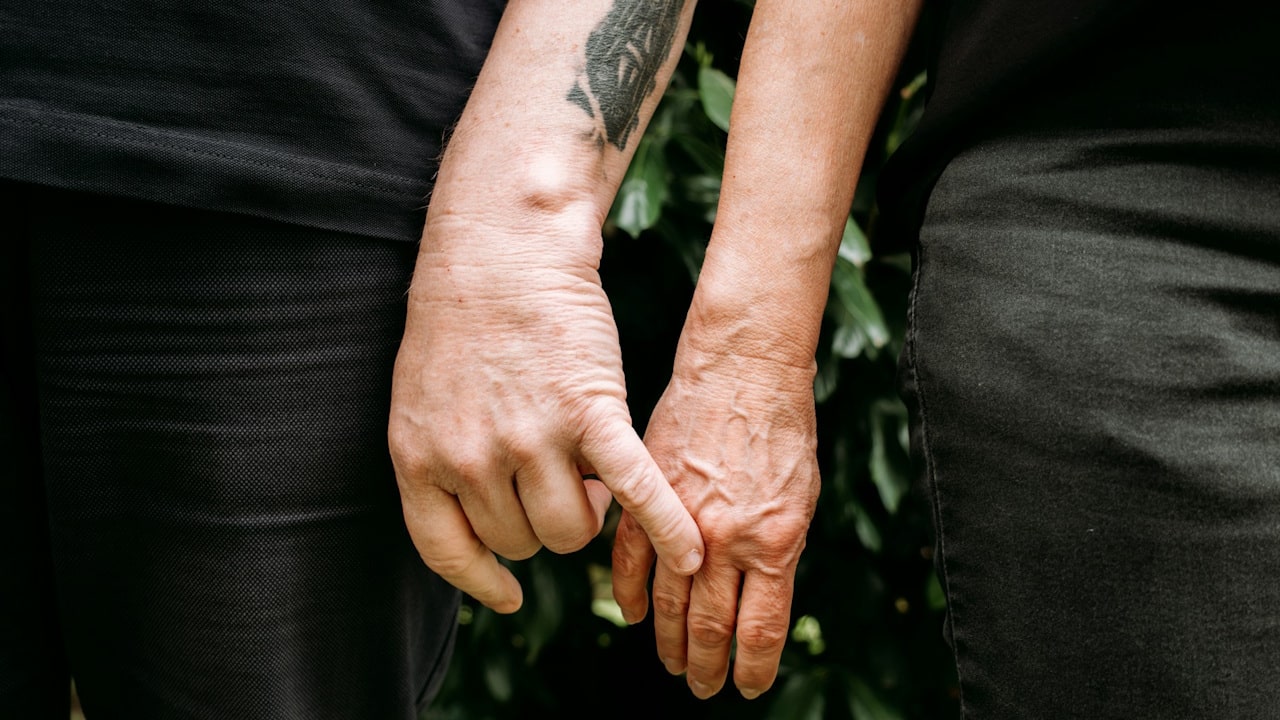 A close-up of two people holding hands by linking their index fingers, with one arm having a tattoo.