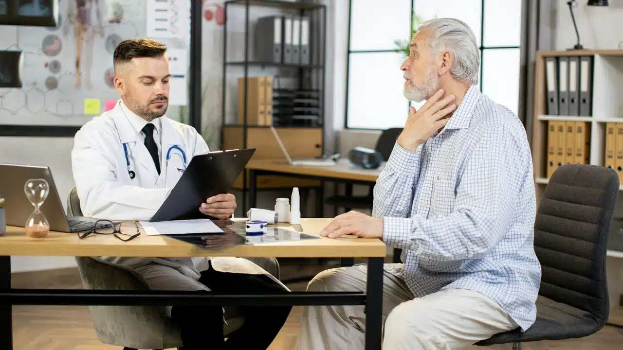 A doctor in a white coat looks at a clipboard while an older man gestures.