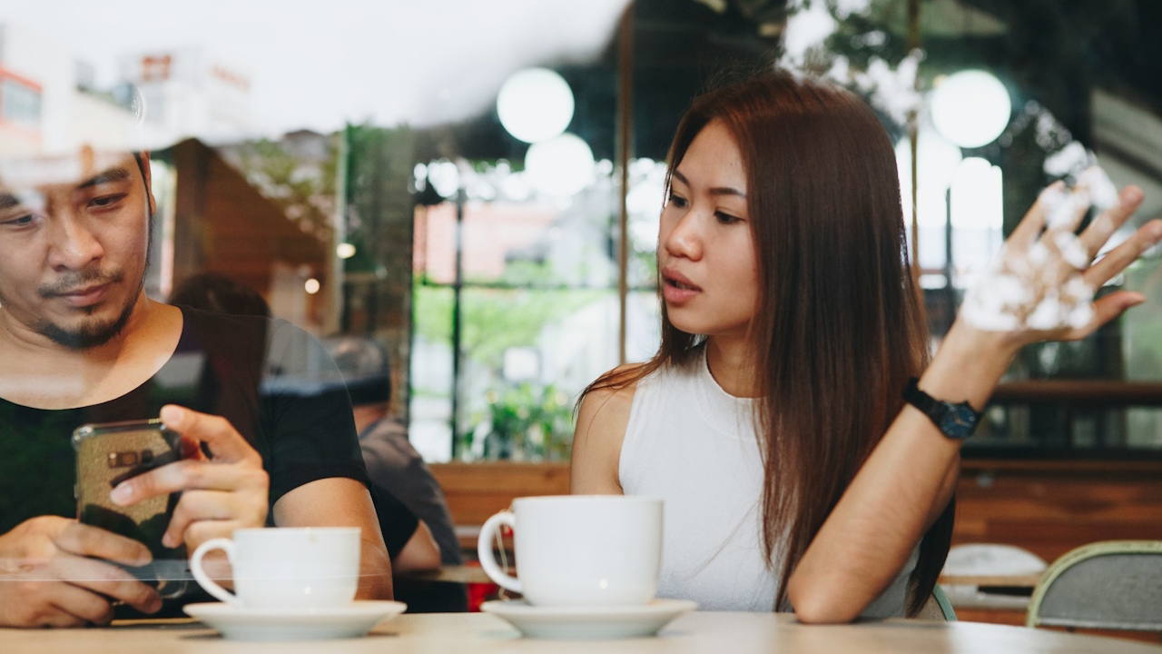 A man is focused on his smartphone while a woman next to him is talking