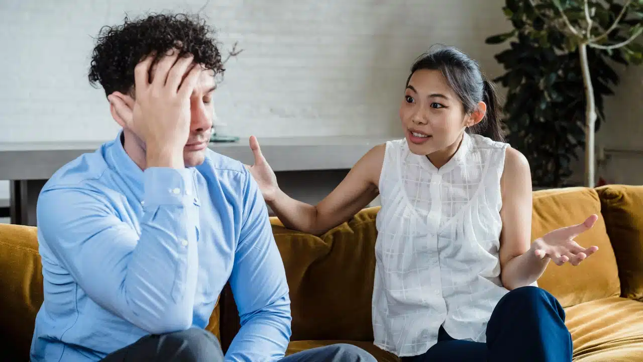 A woman gesturing while speaking to a man who is holding his head in distress.