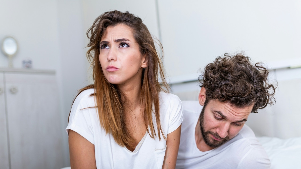 A woman looks upward with a frown while a man sits beside her with eyes downcast.