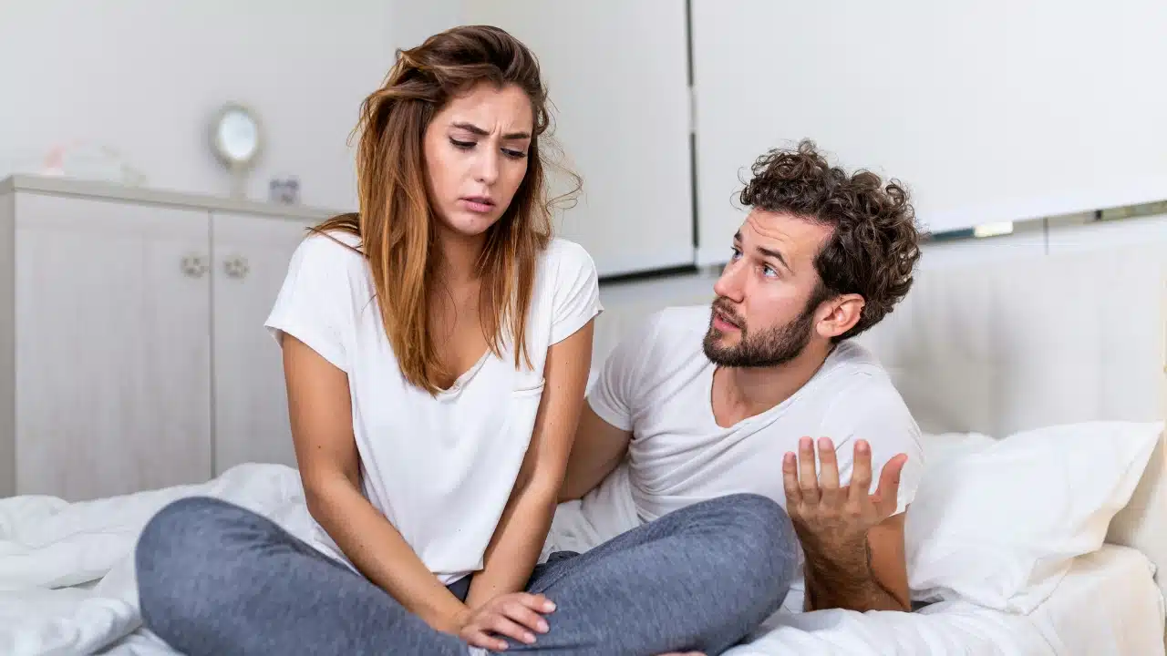 A woman sits with a concerned expression while a man gestures with an open hand.