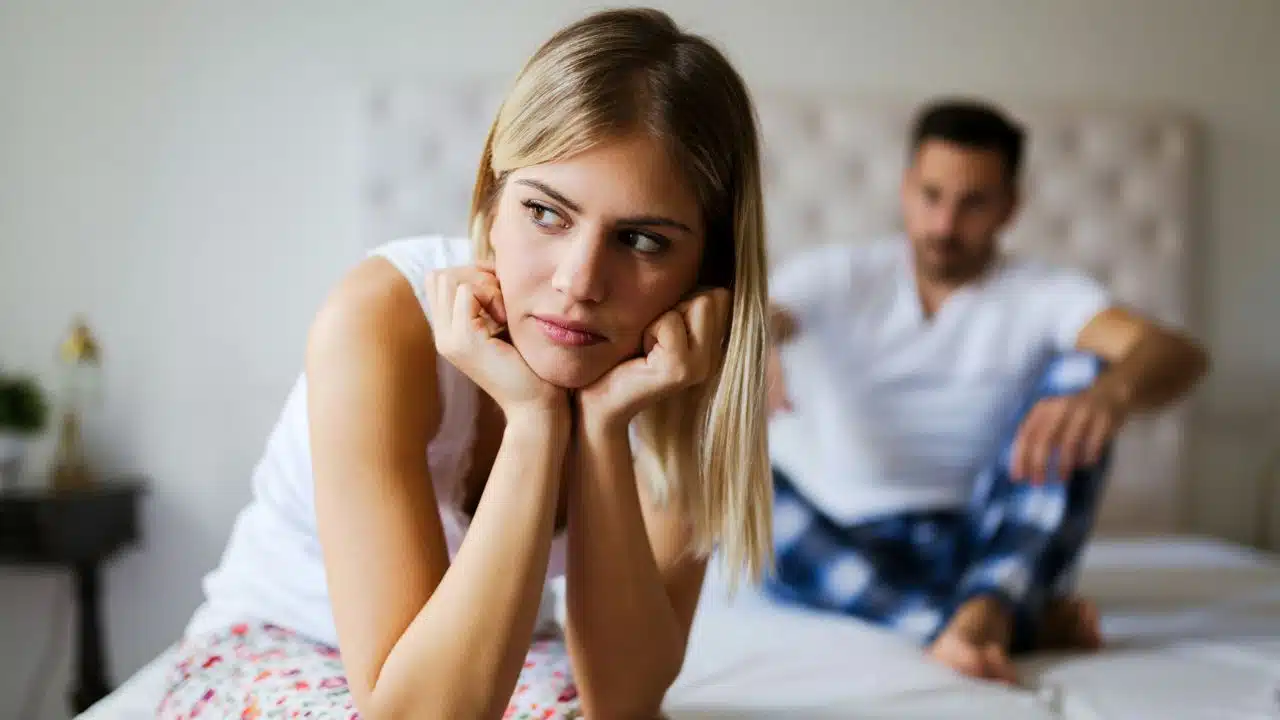 A woman rests her chin on her hands looking sideways while a man sits behind her.